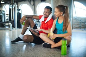 Active man and woman having snack at break between workouts and watching online videos in tablet